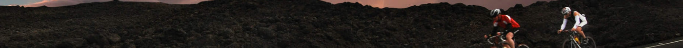 Two cyclists riding on a remote asphalt road with dramatic sunset clouds, demonstrating the importance of carrying a mini bike pump for long-distance adventures.